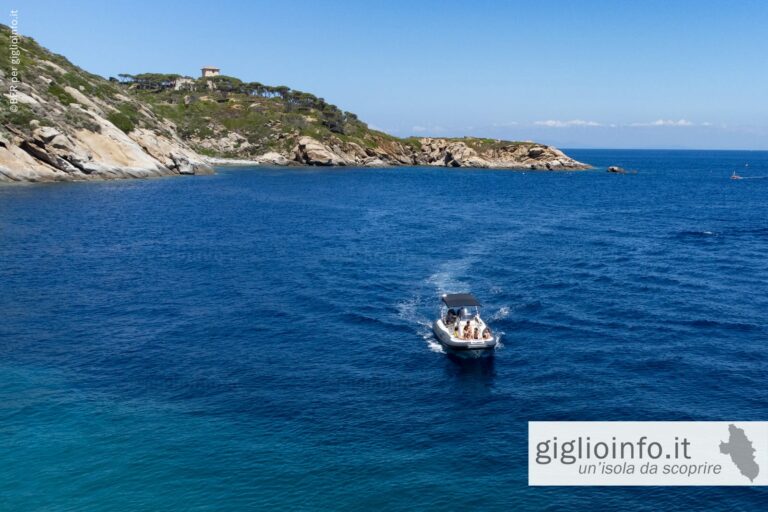 Barca rientra a Giglio Porto con sullo sfondo Torre del Lazzaretto, Isola del Giglio, vista dall'alto con il drone