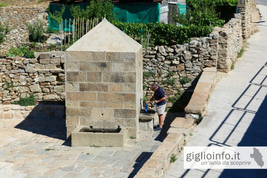 Persona che riempe delle bottiglie alla fontana di acqua potabile a Giglio Castello Sorgente Acqua Selvaggia